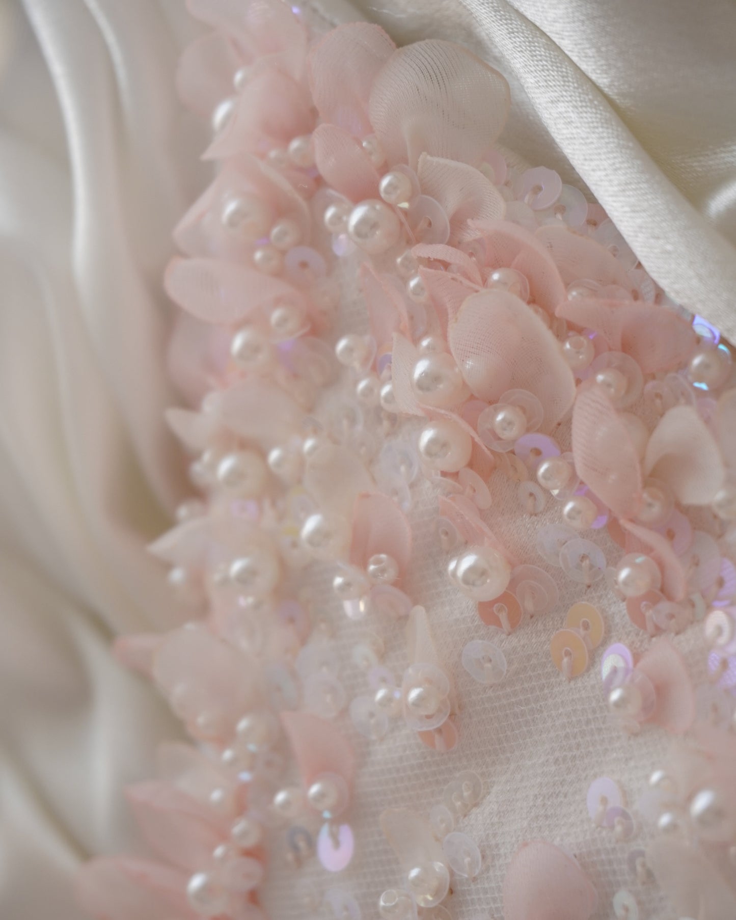 Close-up of pink floral embellishments with pearls on a white fabric background